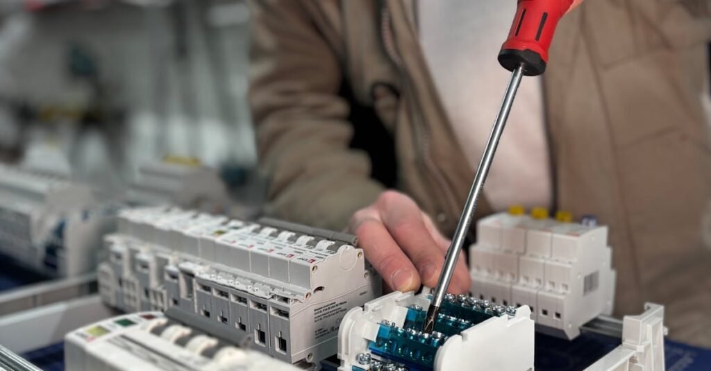 An electrician uses a screwdriver to assemble a circuit board in a well-lit workshop.